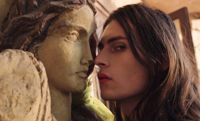 Still from Lulu - A feminine person with long hair puts their face very close to a the face of a statue